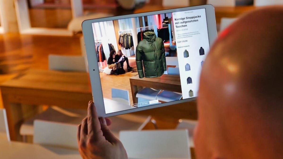 iPad zeigt AR-Ansicht einer grünen Steppjacke mit Produktdetails und Preis in Store-Umgebung